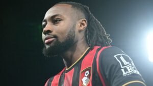 L'ailier de Bournemouth Antoine Semenyo, vêtu du maillot rouge et noir du club, fixe pensivement le regard sous les lumières du stade.
