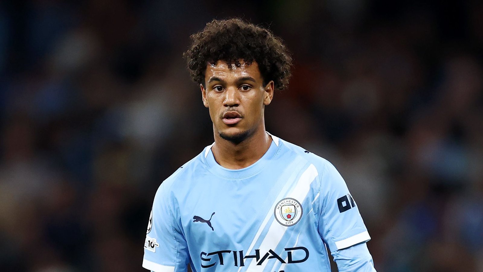 Jonge Manchester City-speler in een lichtblauw tenue, met een geconcentreerde uitdrukking tijdens een wedstrijd, wat zijn mogelijke transfer naar Fulham benadrukt.
