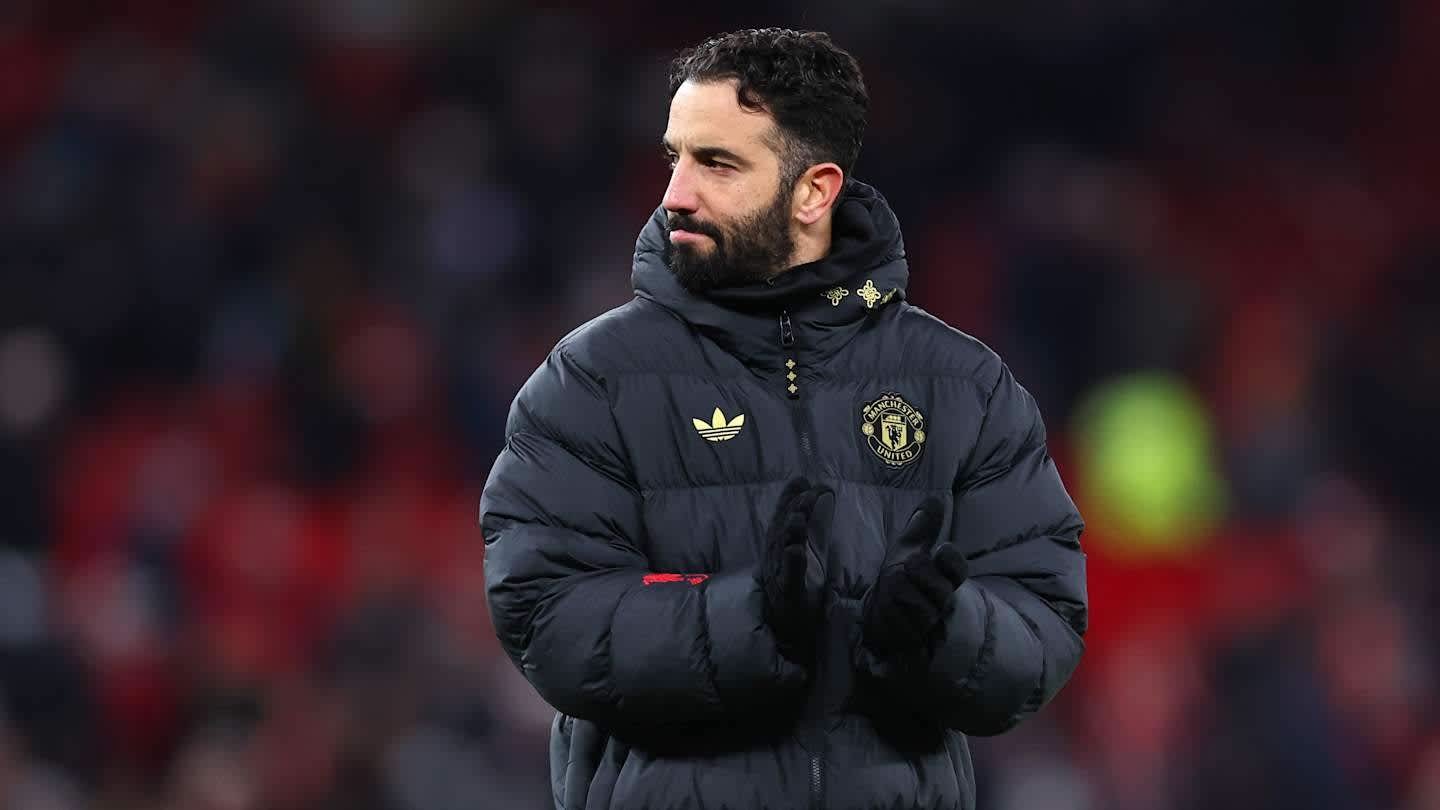 Un membre du personnel de Manchester United, portant une doudoune noire arborant le blason du club, applaudissant en bord de terrain lors d'un match.