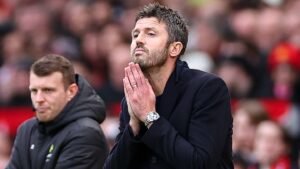 Michael Carrick, deep in thought, clasps his hands at the touchline during a match, with a blurred crowd in the background.