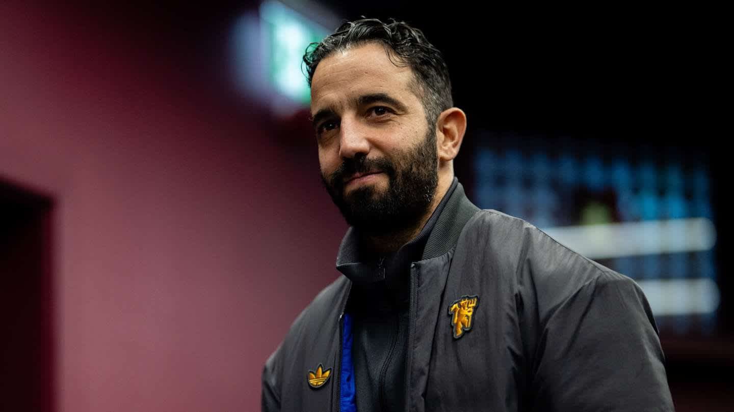Footballeur marocain dans une veste noire avec un logo doré, souriant devant un fond sombre avec un éclairage bleu.