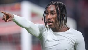 Désiré Doué gesticule avec enthousiasme sur le terrain, portant un haut d'entraînement clair lors d'un match de football.