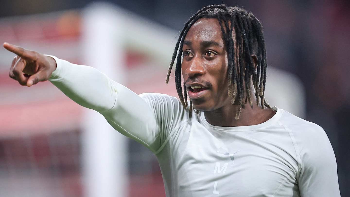 Désiré Doué gesticule avec enthousiasme sur le terrain, portant un haut d'entraînement clair lors d'un match de football.