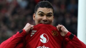 كاسيميرو يحتفل بفرح وهو يرتدي قميص مانشستر يونايتد الأحمر، ماسكًا بأعلى القميص وهو يبتسم في الملعب.