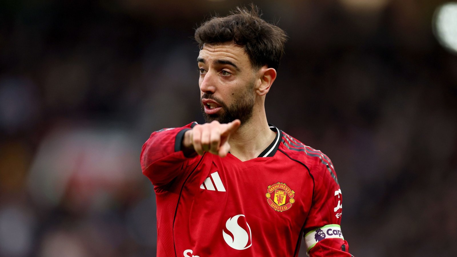 Bruno Fernandes, vêtu du maillot rouge de Manchester United, gesticule avec intensité pendant un match, illustrant son leadership et sa concentration.