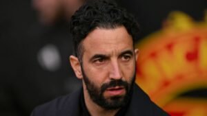 Ruben Amorim, er serieus uitziend, met een vervaagd Manchester United-logo op de achtergrond, wat wijst op managementspanning.