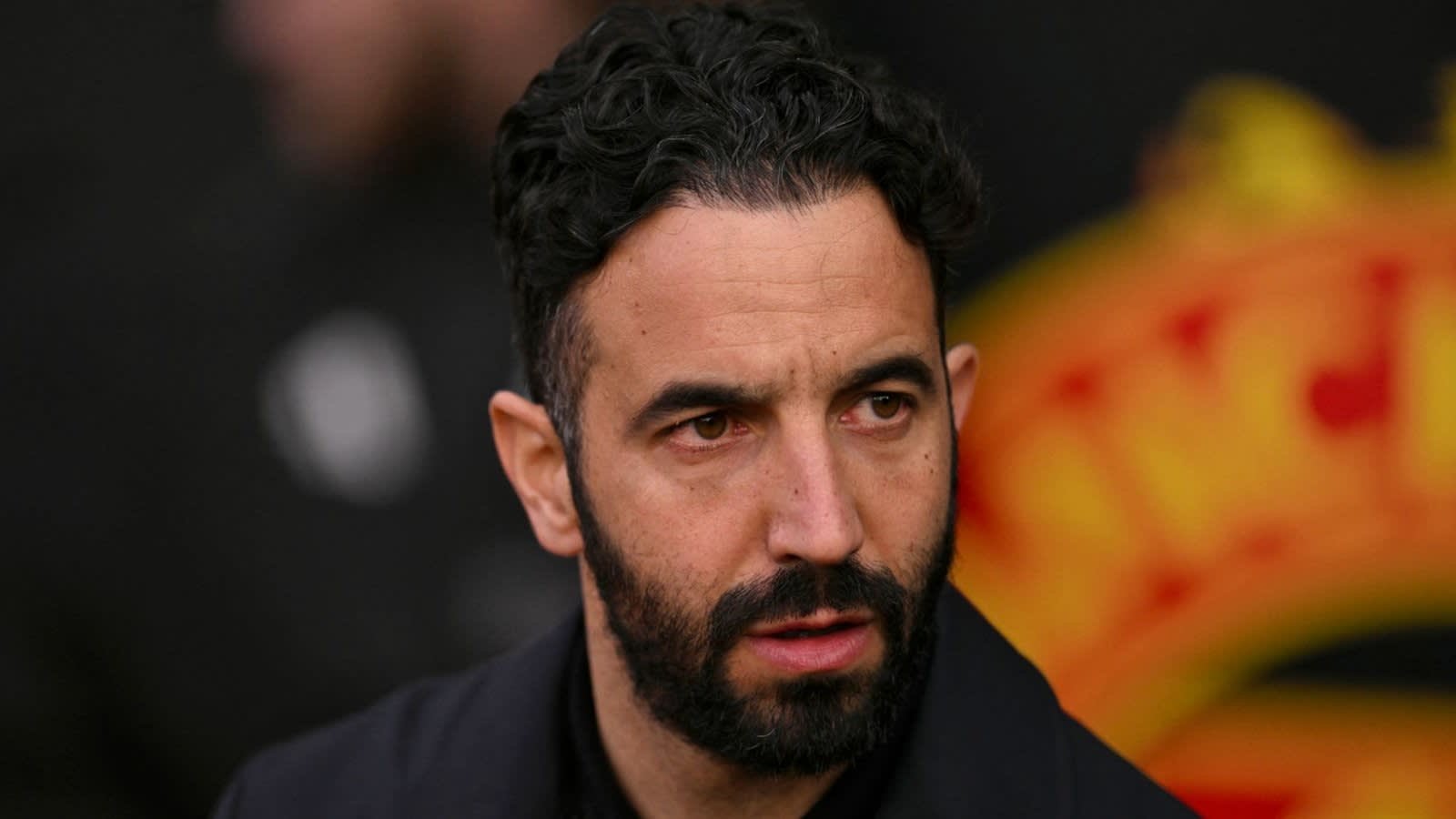Ruben Amorim, er serieus uitziend, met een vervaagd Manchester United-logo op de achtergrond, wat wijst op managementspanning.