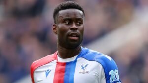 Marc Guehi, portant le maillot rouge et bleu de Crystal Palace, concentré pendant un match, faisant preuve de détermination sur le terrain.
