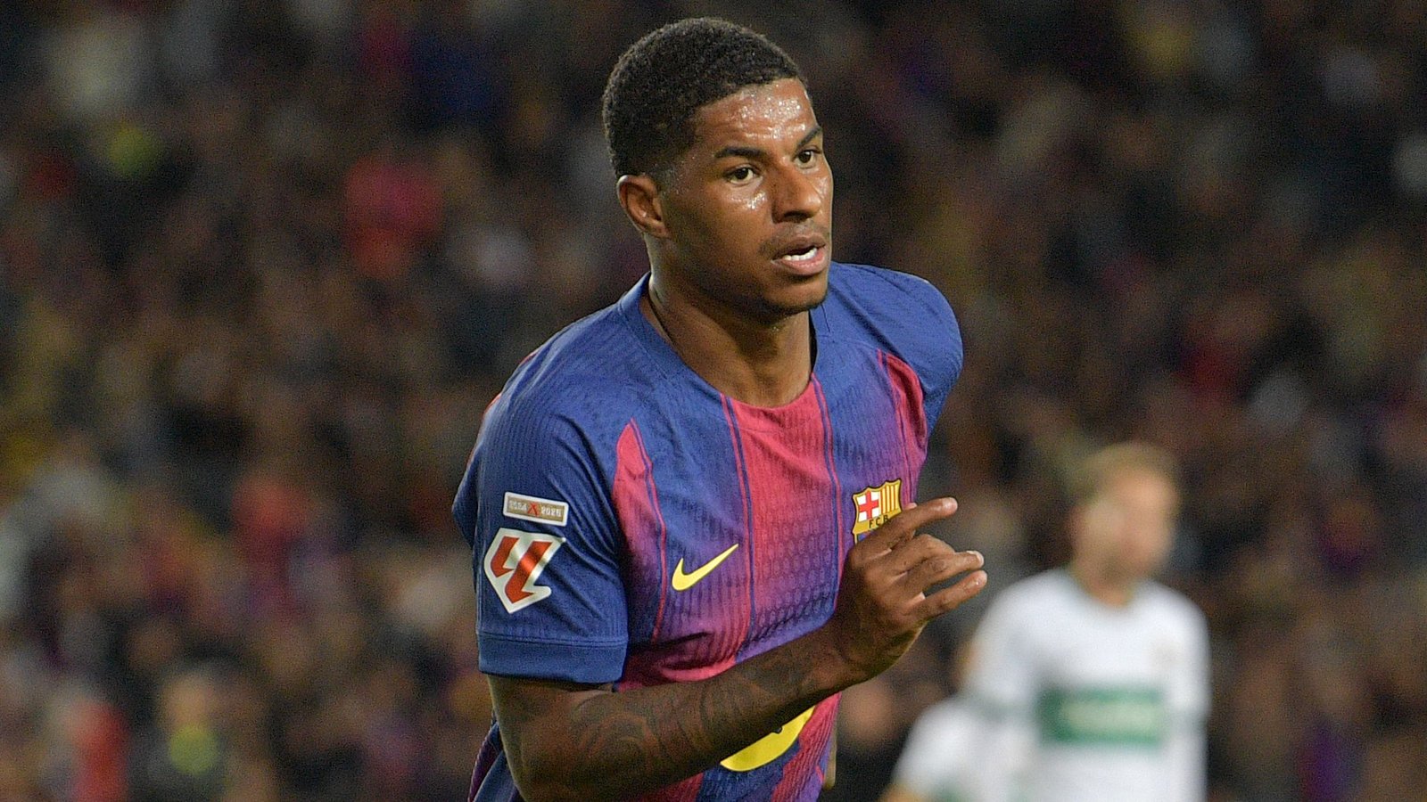 Marcus Rashford in de iconische kastanjebruine en blauwe outfit van Barcelona, gefocust op het spel tijdens een wedstrijd, en toont vastberadenheid op het veld.