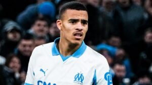 Een Marseille-speler ziet er bezorgd uit tijdens een wedstrijd, gekleed in het wit-blauwe tenue van de club, met wazige fans op de achtergrond.