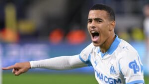 Mason Greenwood viert uitbundig na het scoren van een hattrick, terwijl hij het wit en hemelsblauwe tenue van Marseille draagt tijdens een wedstrijd.