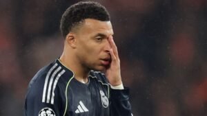 Kylian Mbappé, in een Real Madrid-tenue, toont frustratie tijdens een wedstrijd, met een geconcentreerde uitdrukking en hand aan zijn gezicht.