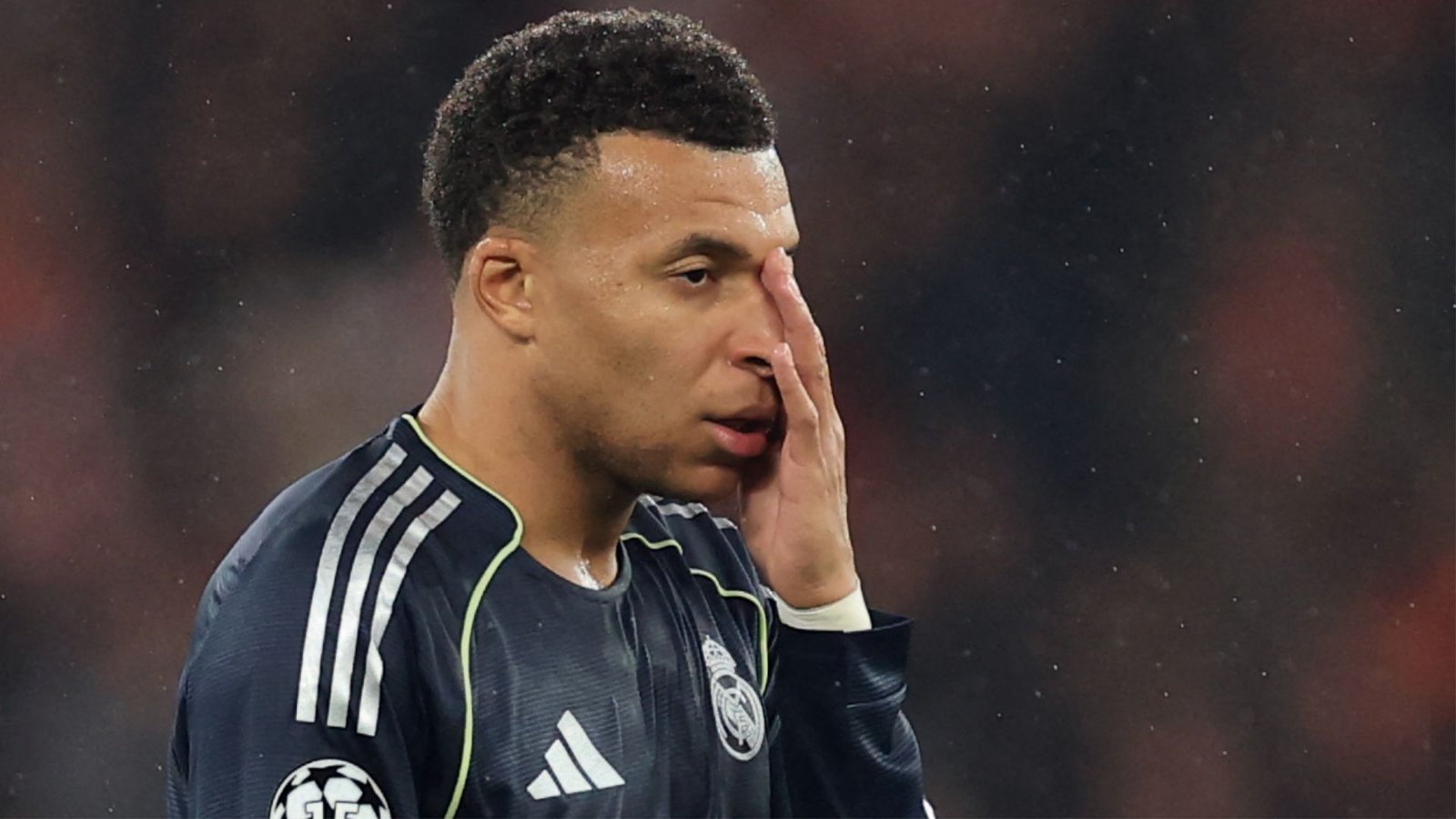 Kylian Mbappé, in een Real Madrid-tenue, toont frustratie tijdens een wedstrijd, met een geconcentreerde uitdrukking en hand aan zijn gezicht.