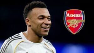 Kylian Mbappé glimlacht in een wit tenue met zwarte accenten, naast het Arsenal-logo, wat op mogelijke transferinteresse wijst.