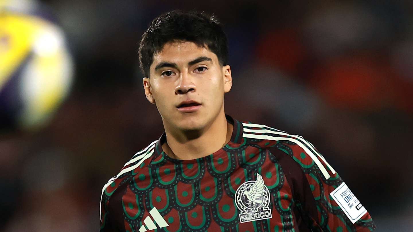 Footballeur mexicain portant un maillot distinct maroon et vert, concentré sur le match, avec un arrière-plan de stade flou.