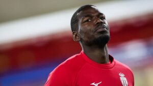 Paul Pogba in een rood AS Monaco-trainingspak, peinzend, reflecteert op zijn blessuretegenslagen tijdens het 2026-seizoen.