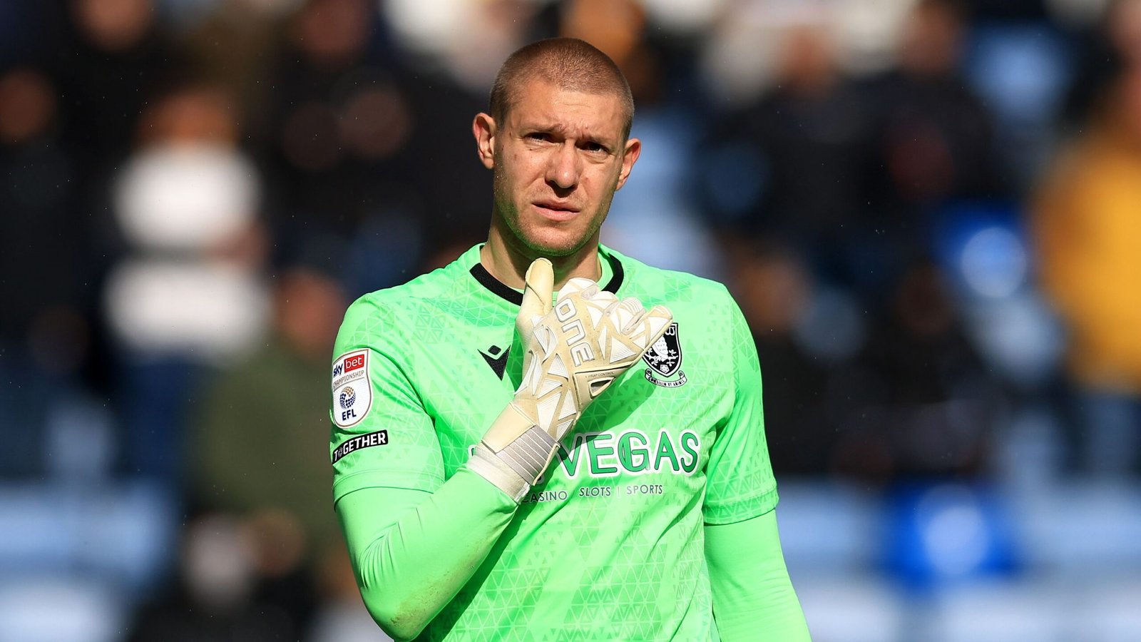 Ethan Horvath in een felgroen keepers-tenue, gebarend met zijn gehandschoende hand tijdens een wedstrijd, met wazige fans op de achtergrond.