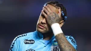 Neymar in een blauw voetbaltenue, zichtbaar aangedaan, met zijn hand op zijn gezicht, waarbij zijn getatoeëerde armen en gevlochten haar te zien zijn.