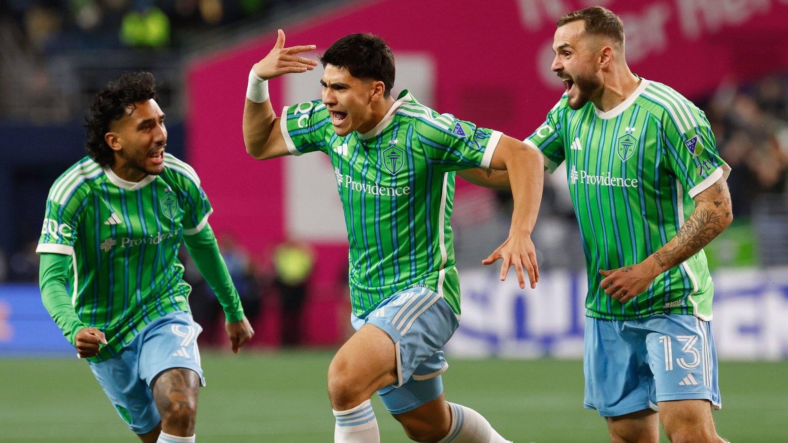 Les joueurs des Seattle Sounders célèbrent un but, vêtus de leurs tenues vert et bleu vif, illustrant l'enthousiasme dans l'atmosphère animée du stade.