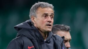 Luis Enrique in een donkere hoodie, peinzend tijdens een trainingssessie, met een wazig veld op de achtergrond, wat zijn focus op PSG weerspiegelt.
