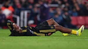 Patrick Dorgu lies on the pitch, clutching his forehead in distress, wearing a black and yellow kit during a match.