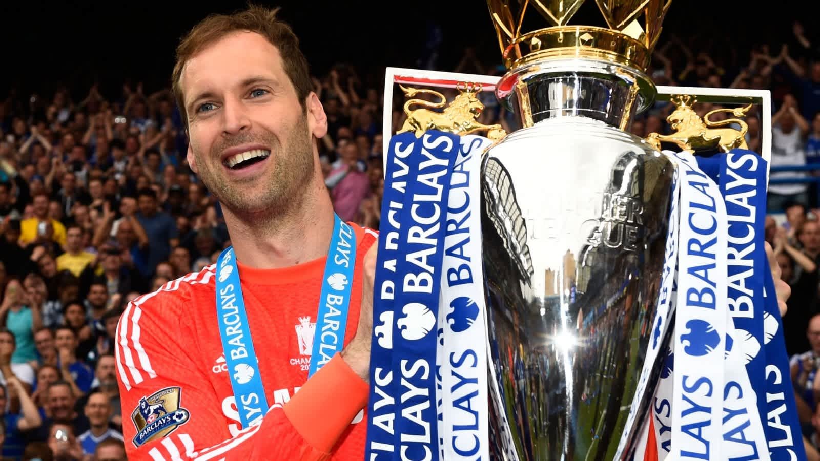 Petr Čech célèbre avec le trophée de Premier League, vêtu de sa tenue de gardien de but, au milieu d'une foule en liesse. Des rubans bleus et blancs ornent le trophée.