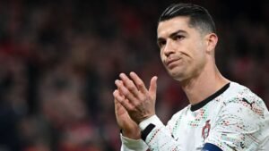 Cristiano Ronaldo applaudisseert voor fans in een witte Portugal-outfit met kleurrijke ontwerpen, met een gemengde uitdrukking tijdens een wedstrijd.