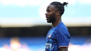 Raheem Sterling in a blue Chelsea kit, focused during a match, showcasing his determination on the pitch.
