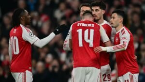 Arsenal-spelers vieren een doelpunt, met shirts in rood en wit, waarop de nummers 10 en 14 zichtbaar zijn, wat teamwork in een cruciale wedstrijd benadrukt.