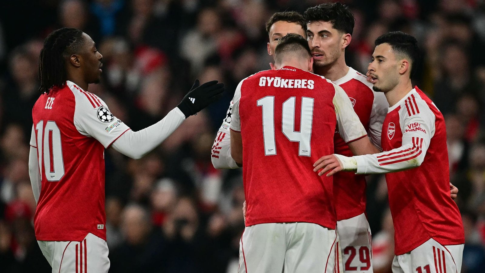 Arsenal-spelers vieren een doelpunt, met shirts in rood en wit, waarop de nummers 10 en 14 zichtbaar zijn, wat teamwork in een cruciale wedstrijd benadrukt.