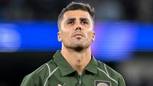Rodri, wearing a green Manchester City jacket, gazes upwards with a serious expression, showcasing his determination before a match.