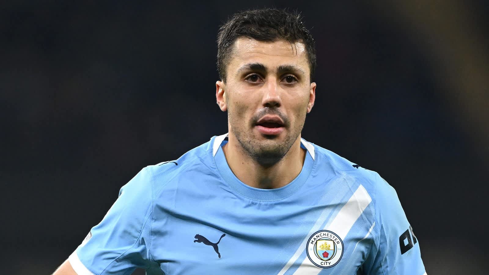 Rodri portant le maillot bleu clair de Manchester City, l'expression concentrée sur son visage pendant un match, démontrant détermination et talent.