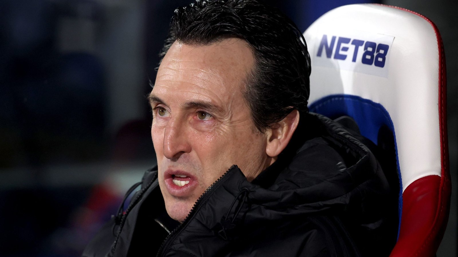 Unai Emery, l'entraîneur d'Aston Villa, concentré et animé en bord de terrain pendant un match, portant un manteau noir avec les couleurs de l'équipe en arrière-plan.