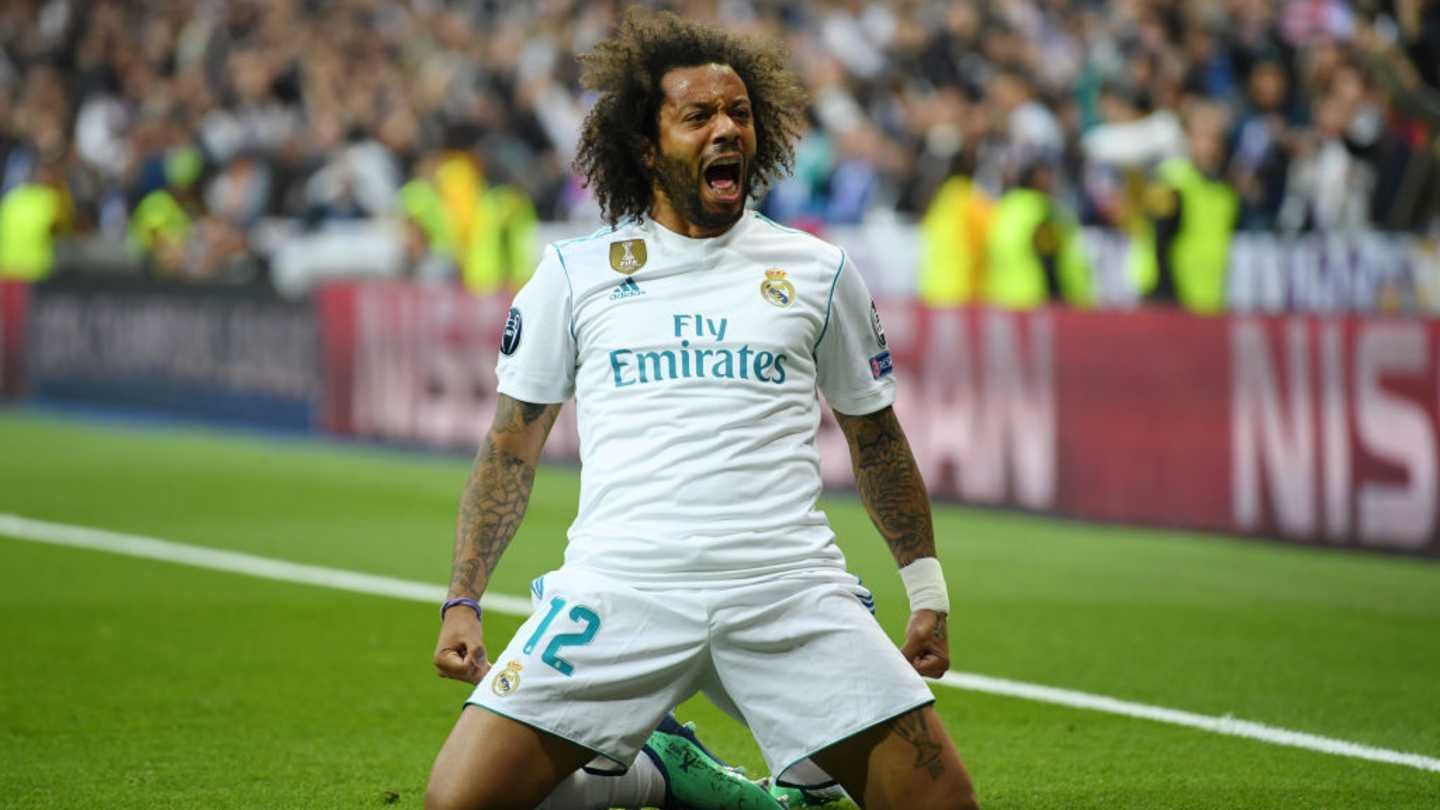 Marcelo celebrates passionately on the pitch in a white Real Madrid kit, surrounded by a vibrant crowd during a Champions League match.
