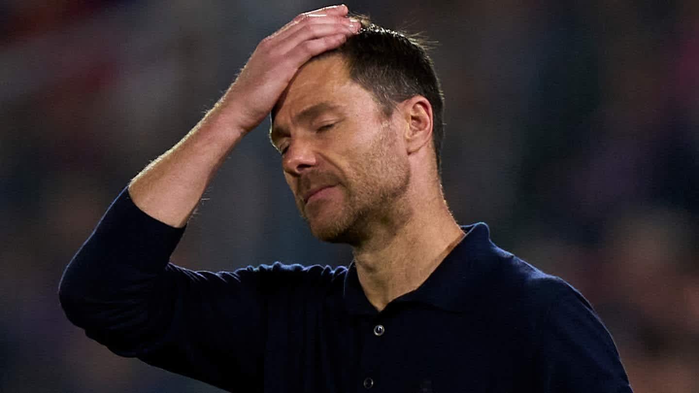 L'entraîneur déprimé se tient le front avec frustration pendant un moment tendu sur la touche, portant un polo bleu foncé.