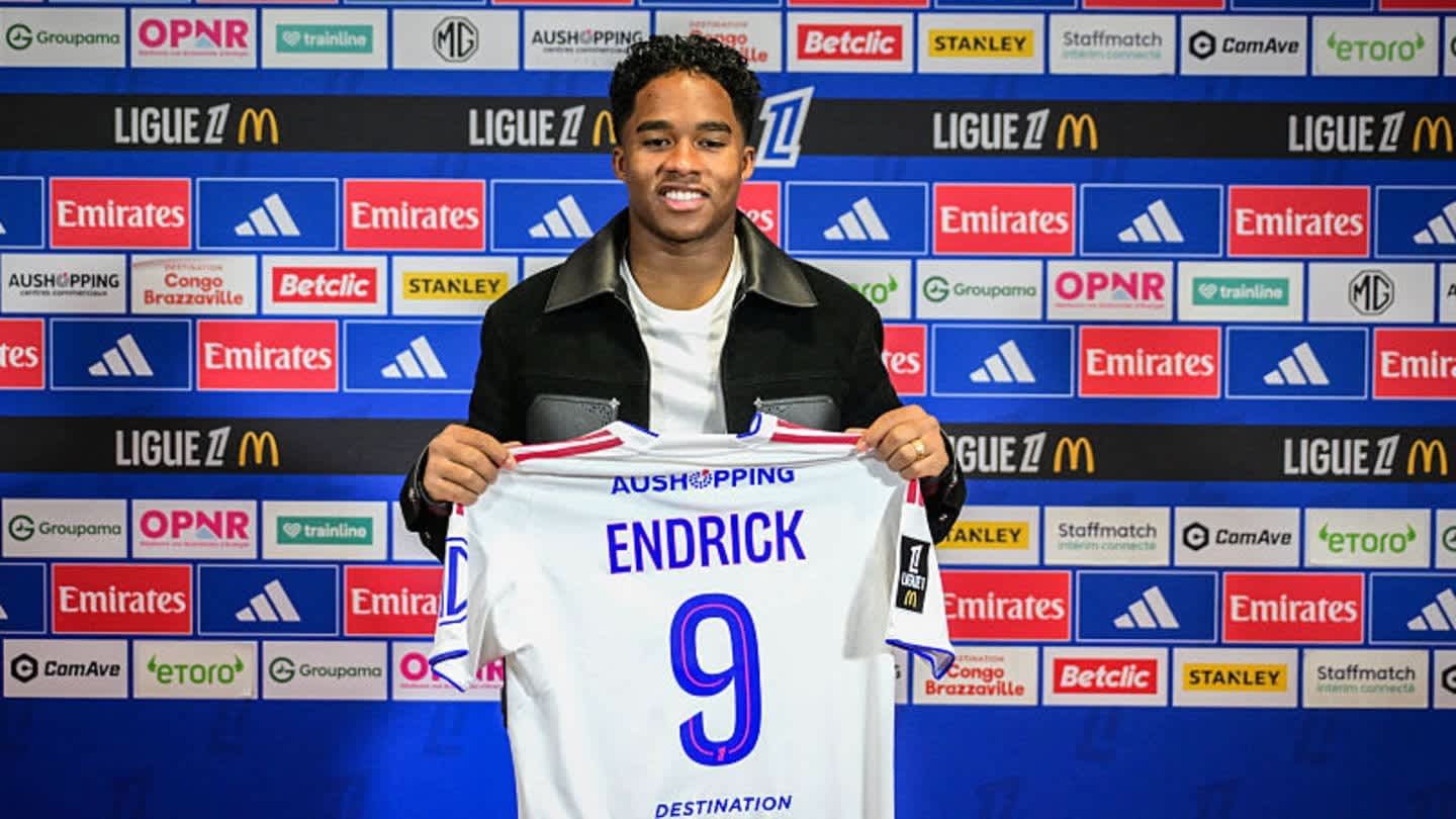 Endrick holds his new team jersey, displaying the name "ENDRICK" and the number "9", with a colourful backdrop featuring sponsor logos.