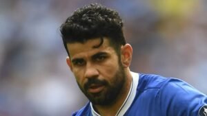 Diego Costa, die een blauw shirt draagt, staart intens naar de camera, wat zijn vastberadenheid op het veld benadrukt.