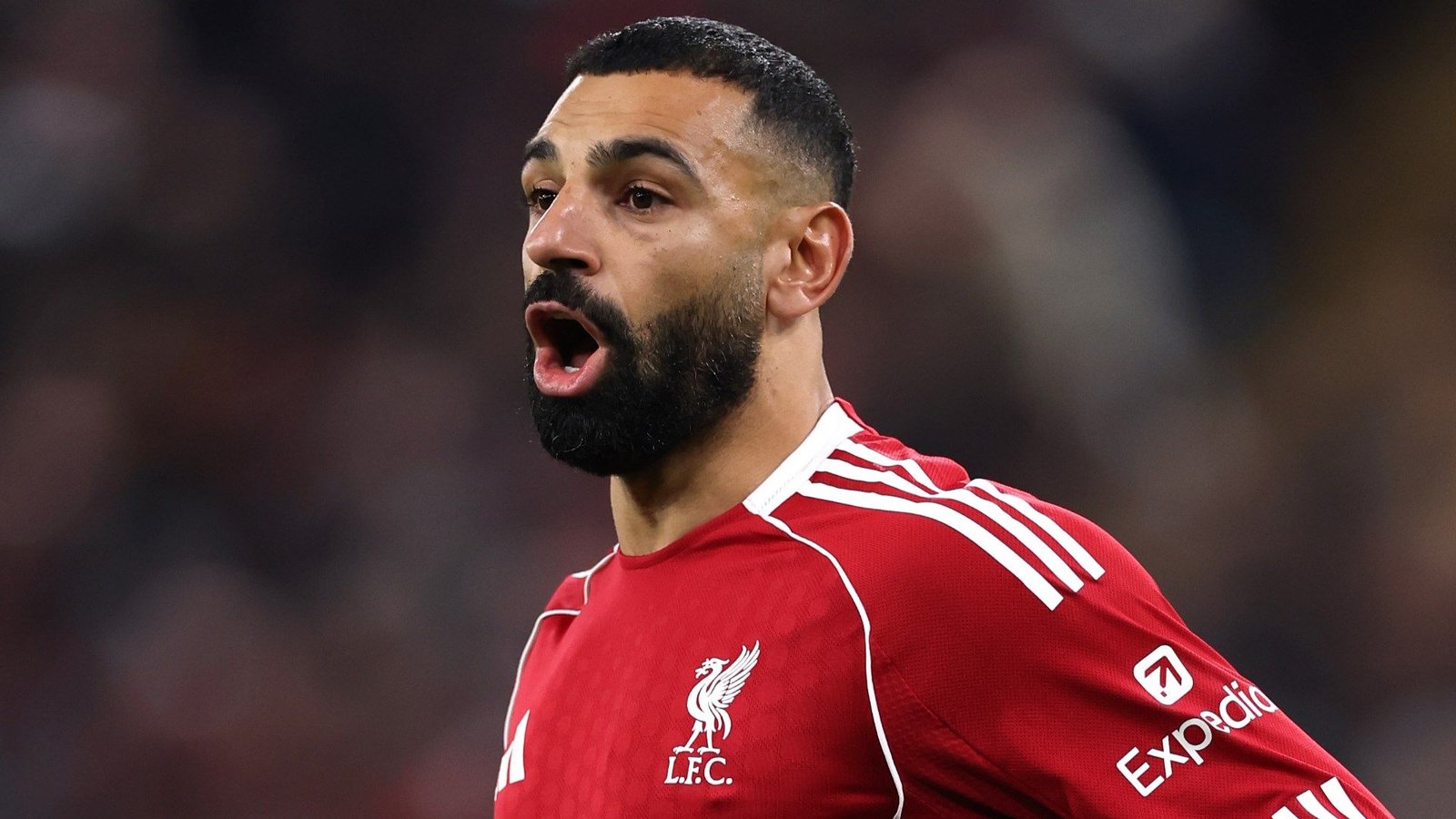 Mohamed Salah die schreeuwt in Liverpool's rode tenue, vol passie tijdens een wedstrijd, belichaamt de intensiteit van het Premier League-voetbal.