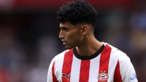 Ricardo Pepi portant le maillot du PSV Eindhoven, aux rayures rouges et blanches, fixant pensivement le terrain pendant un match, son profil étant mis en avant.