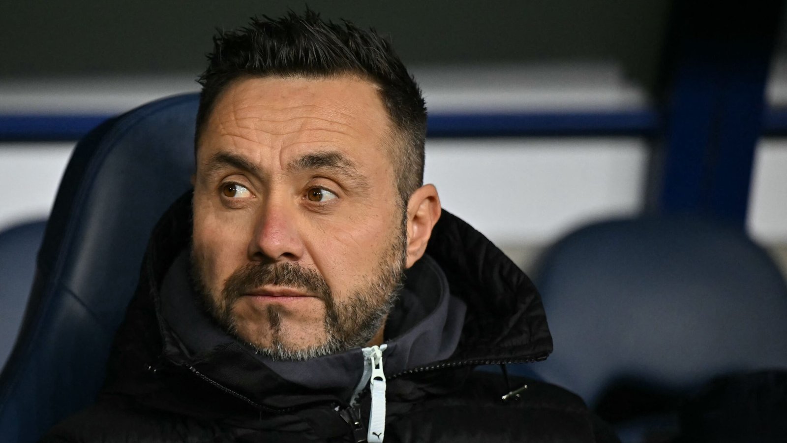 Roberto De Zerbi zit peinzend op de bank van Marseille, gekleed in een zwart jasje, in reflectie na de UCL-uitschakeling.