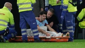 Geblesseerde voetballer die medische hulp krijgt op een brancard, omringd door paramedici in veiligheidshesjes, tijdens een wedstrijd.