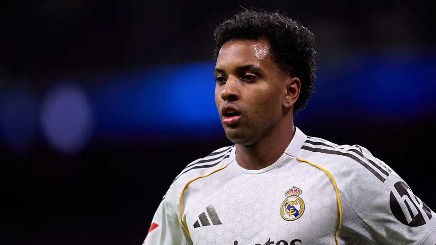Rodrygo, portant un maillot du Real Madrid avec des accents noirs et jaunes, paraît concentré pendant un match, devant un fond de stade flou.