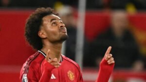 Joshua Zirkzee célébrant avec un doigt levé, portant un maillot rouge de Manchester United dans un stade illuminé.