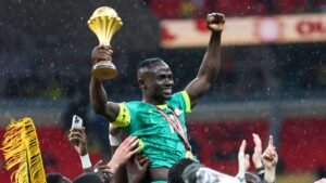 Sadio Mané vierde triomfantelijk, terwijl hij de Afrika Cup-trofee omhooghief, omringd door uitgelaten teamgenoten in een doorweekt stadion.