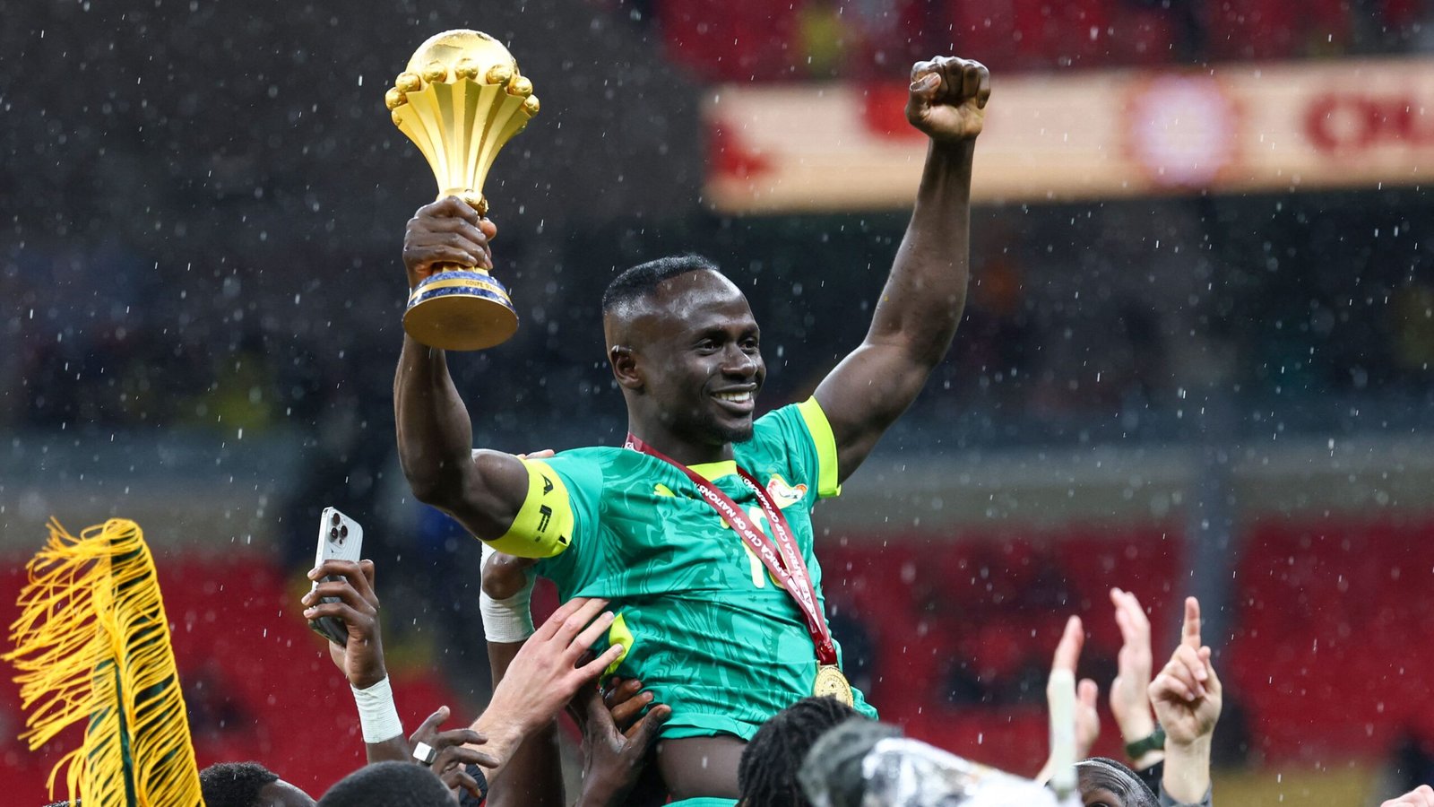 Sadio Mané vierde triomfantelijk, terwijl hij de Afrika Cup-trofee omhooghief, omringd door uitgelaten teamgenoten in een doorweekt stadion.