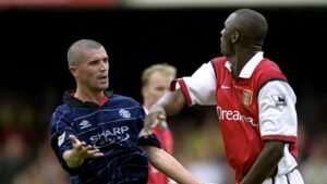 Roy Keane, in het tenue van Manchester United, gebaart levendig, terwijl Patrick Vieira, gekleed in het shirt van Arsenal, hem confronteert in een gespannen moment.