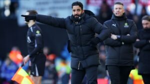 Ruben Amorim gesticule avec passion lors d'un match, portant un manteau noir, avec le personnel d'entraîneurs et les joueurs en arrière-plan.