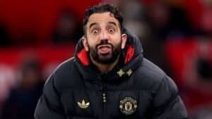 Ruben Amorim, vêtu d'une veste noire de Manchester United, affiche une expression surprise durant un match, illustrant les émotions intenses sur le bord du terrain.