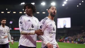 Leeds United-spelers vieren een doelpunt, dragen hun witte uittenue met paarse accenten. Opwinding is zichtbaar op hun gezichten in een vol stadion.