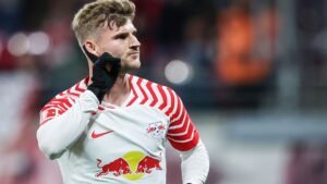 Timo Werner celebrates after scoring, wearing RB Leipzig's white and red kit with a Red Bull logo, showcasing his distinctive hairstyle.